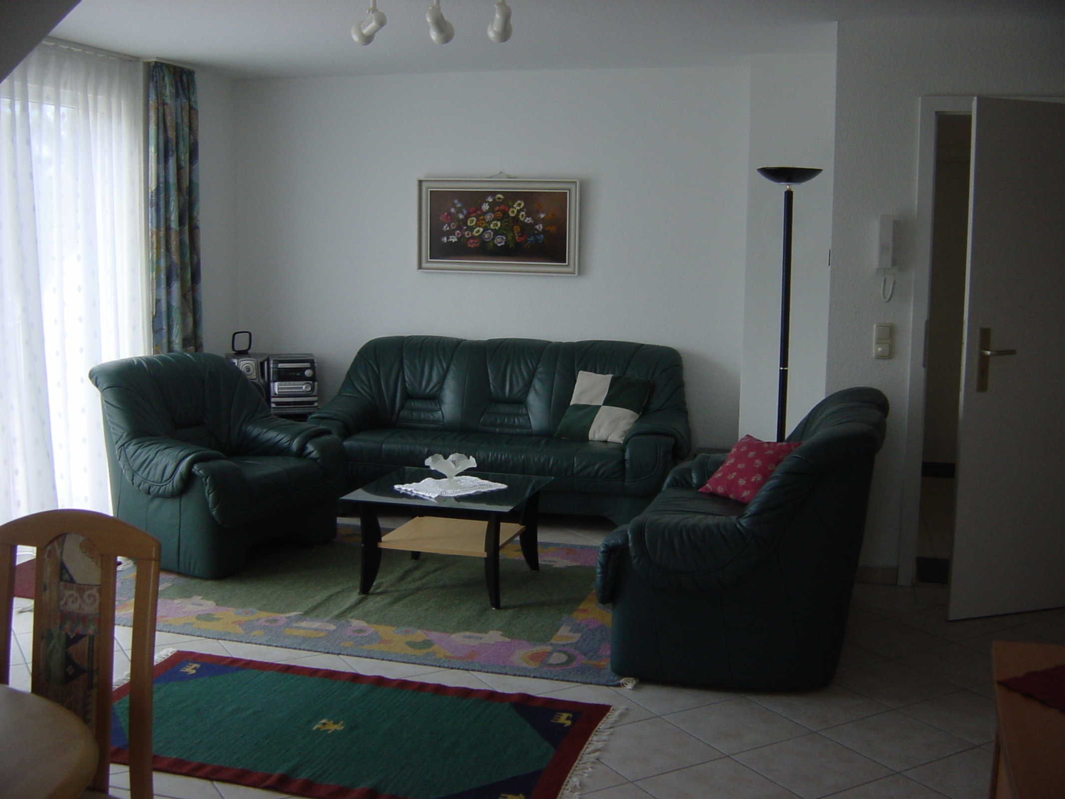 Ein Wohnzimmer mit einem grünen Sofa, einem Couchtisch, einem gemusterten Teppich und einem Bild an der Wand.