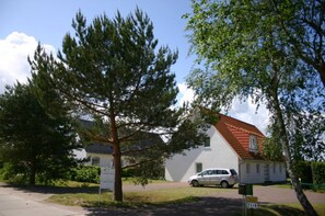 Un bâtiment blanc avec un toit rouge, entouré d’arbres et avec une voiture garée à proximité.