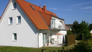 Ein zweigeschossiges Haus mit rotem Dach, einem Balkon und einer kleinen Terrasse.