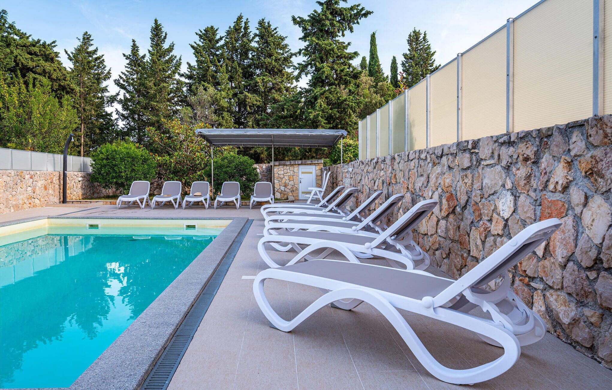 A swimming pool with lounge chairs and a stone wall.