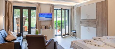 A modern hotel room with a sofa, a bed, a TV, and a balcony with a view of greenery.