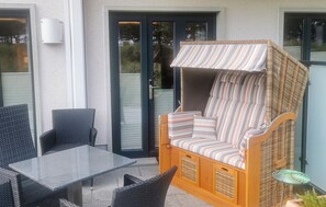 An outdoor seating area with wicker furniture, a striped cushioned sofa, and a glass table. - Stunning apartment in Binz with outdoor swimming pool (Prora/Rügen)