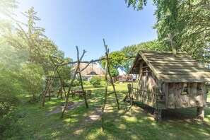 A rustic wooden structure with a thatched roof, surrounded by a lush green garden with a swing set.