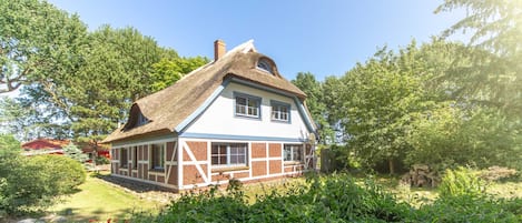 A traditional house with a thatched roof, surrounded by lush greenery.