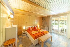 Une pièce comprenant un lit, des tables de chevet, un petit tabouret, un banc et une vue sur un espace extérieur, accessible par une porte vitrée.