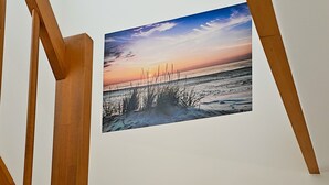 Una obra de arte enmarco que muestra un atardecer sobre una playa con arena y pasto.