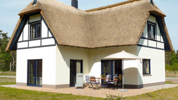Una casa con un techo de paja distintivo, amplias ventanas y un patio con mobiliario exterior.