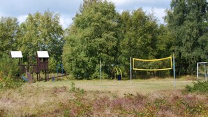 En legeplads med gyngestativ, klatrestrukturer og et gult, netindhegnet område.