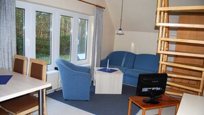 Et værelse med en blå sofa, et lille hvidt bord, et tv-bord i træ og et spisebord med stole.