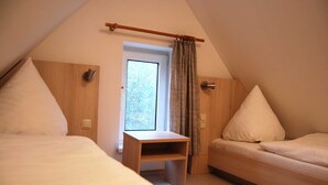 Et soveværelse med to senge, et trænatbord, et vindue med gardiner og en dør.