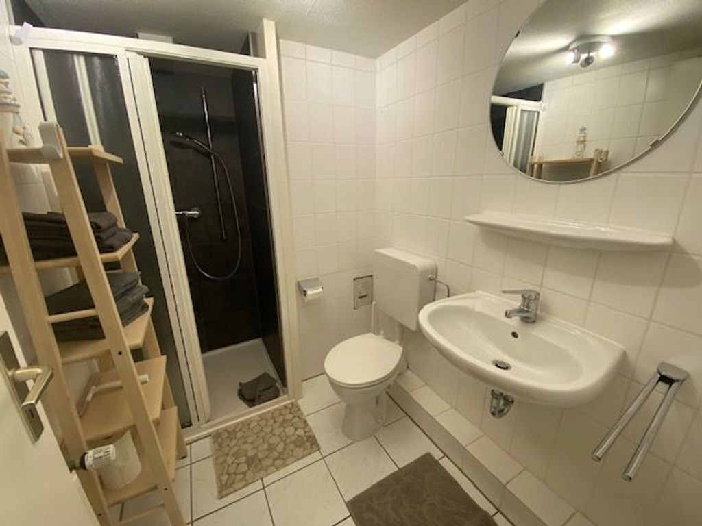 Ein Badezimmer mit Toilette, Waschbecken und Dusche. An der Wand befinden sich ein Handtuchhalter und ein Spiegel.
