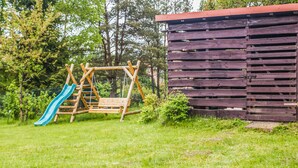 Une aire de jeux avec des balançoires et un toboggan, une clôture en bois et un bâtiment aux murs à lattes.