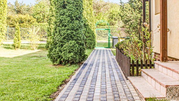 Un chemin pavé mène à un bâtiment entouré d’une clôture en bois et doté d’un portail vert.