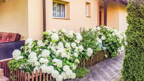 Un bâtiment à la façade jaune, avec une clôture en bois et des arbustes d’hortensias blancs.