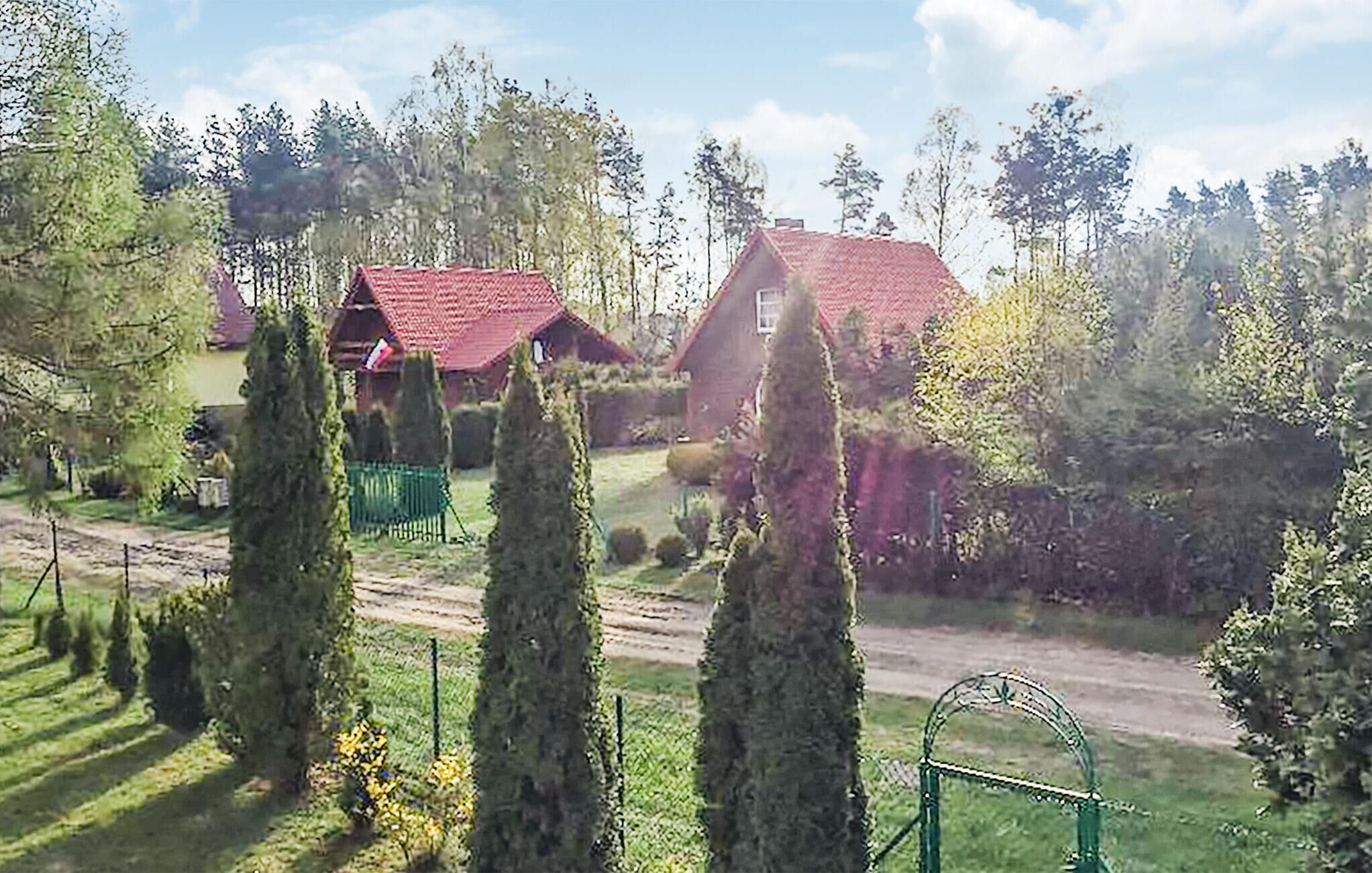 Ländliche Landschaft mit einem rotem Haus, umgeben von Bäumen und einem grünen Tor.