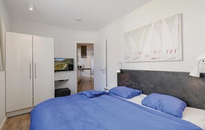 Een slaapkamer met een bed, een kledingkast, een televisie en een schilderij aan de muur.