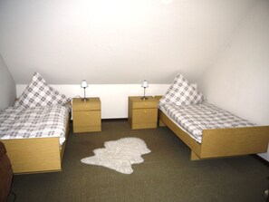 A small, single-room with two wooden beds, each with a matching nightstand and lamp, and a white furry rug on the floor.
