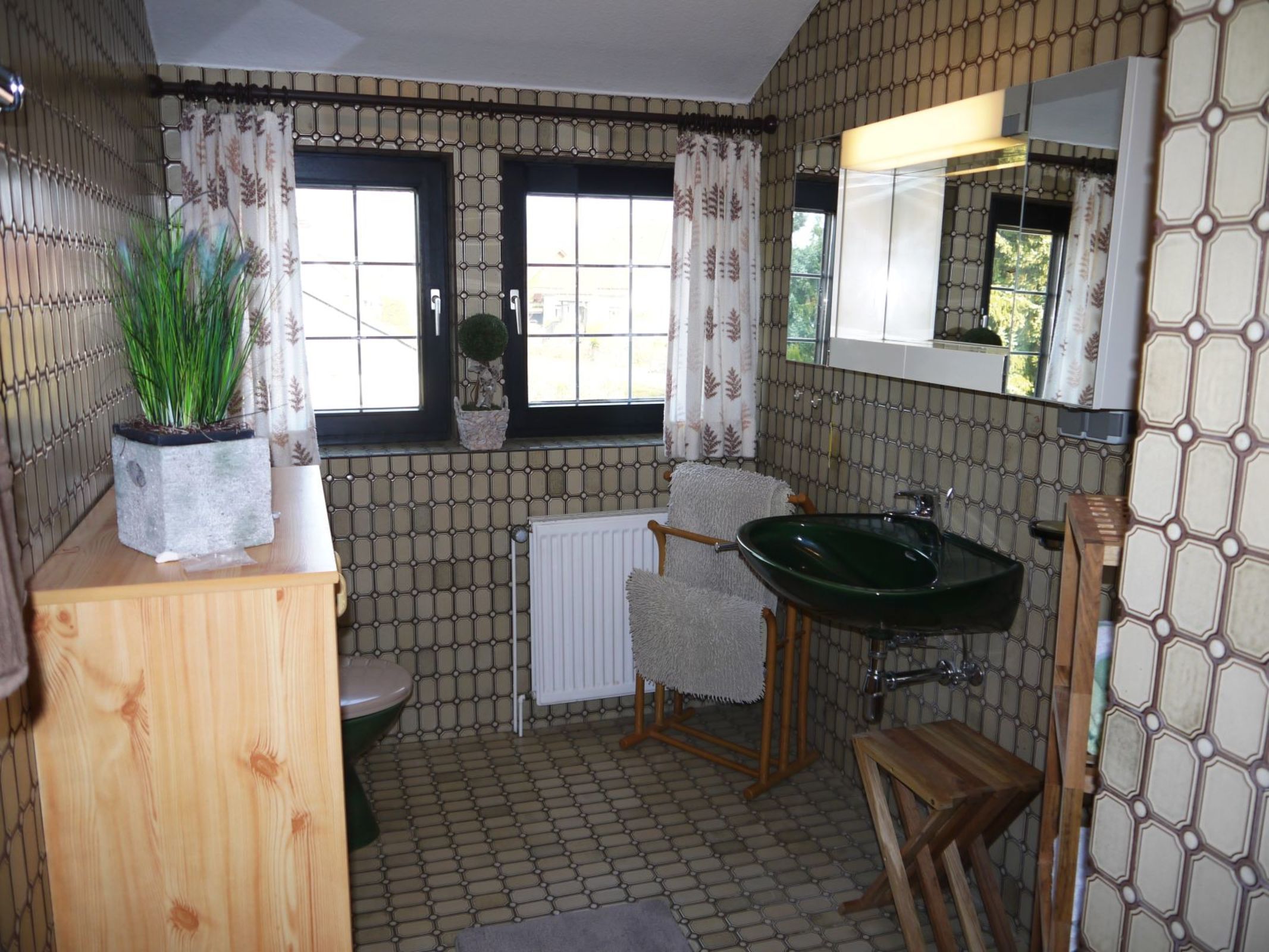 A bathroom with a green sink, a toilet, a towel rack, and a potted plant.