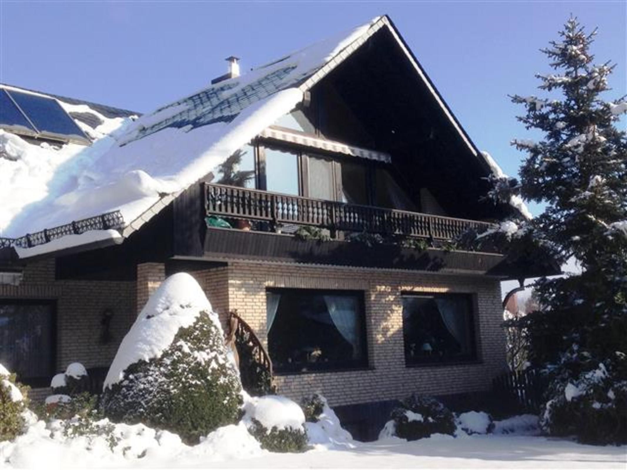 Una casa de dos pisos con techo inclinado, un balcón con barandillas y una chimenea.