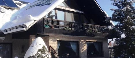 Una casa de dos pisos con techo inclinado, un balcón con barandillas y una chimenea.