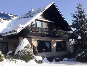 A two-story house with a sloped roof, a balcony with railings, and a chimney.