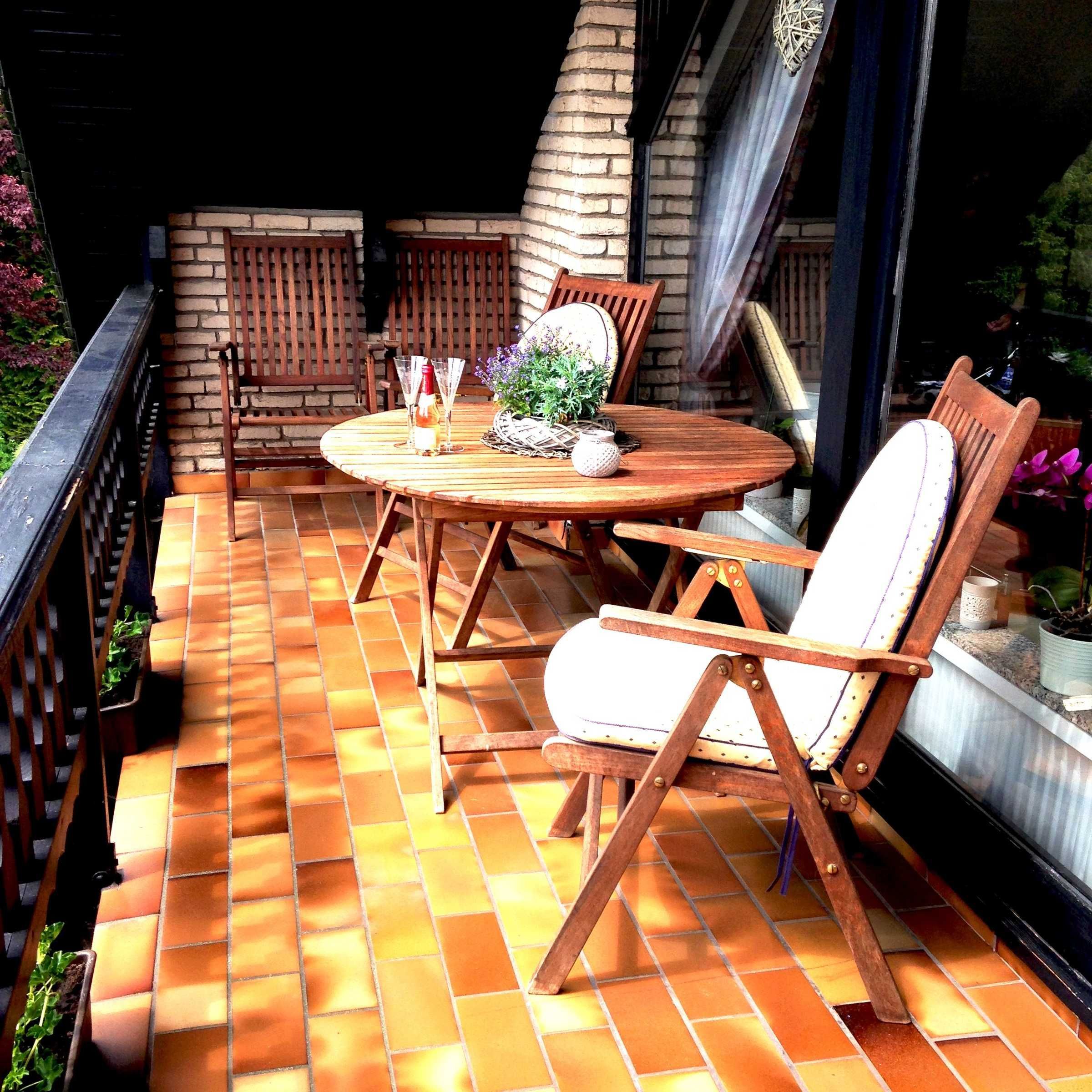 A wooden table and chairs on a tiled patio with a brick wall and window.