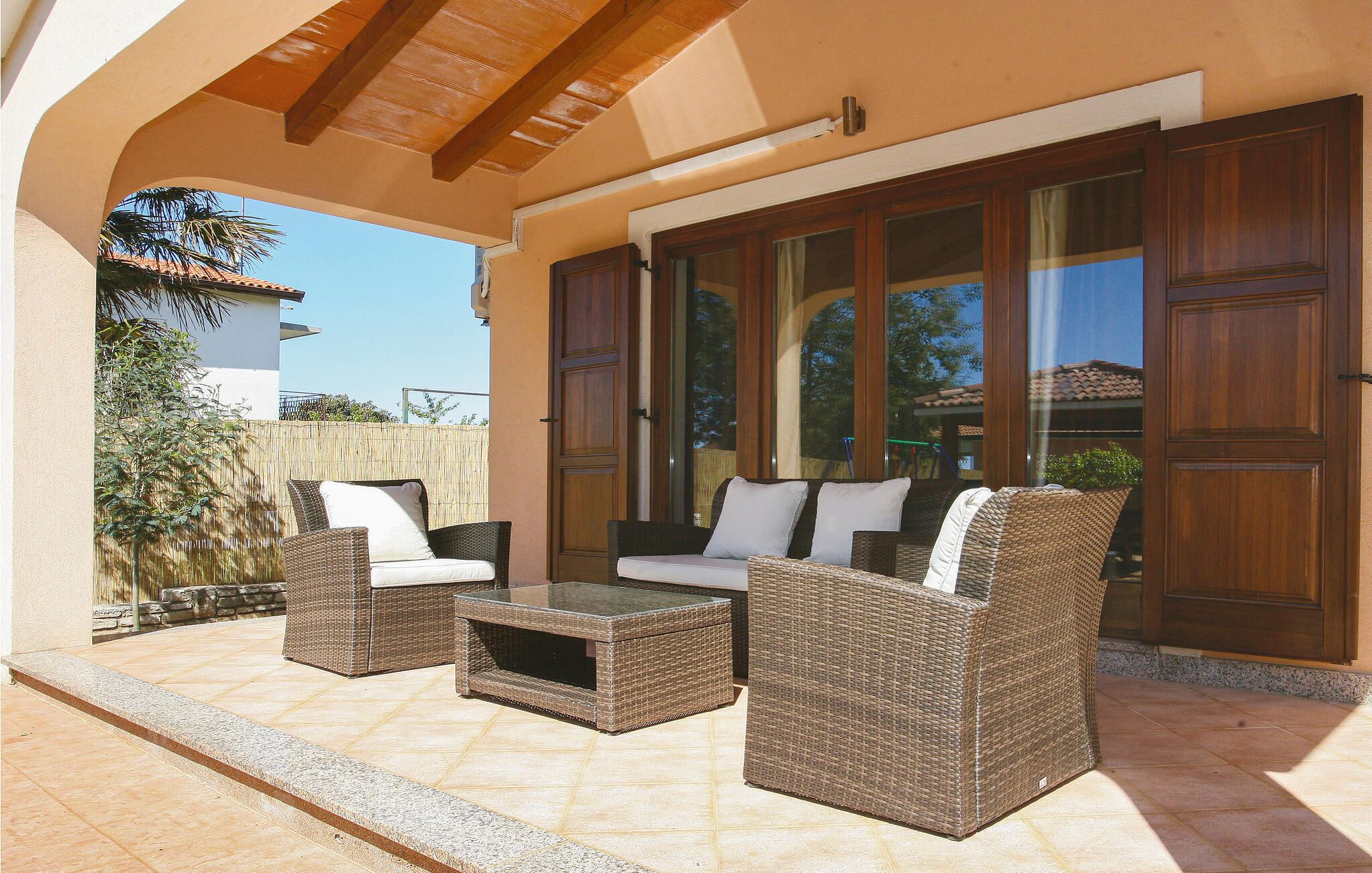 Un patio al aire libre con mobiliario de mimbre, un ventanal de vidrio y vistas del entorno.