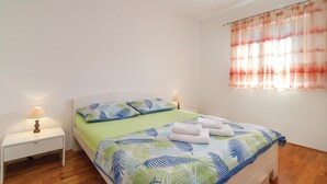 Un dormitorio con cama, mesita de noche, lámpara y ventana con cortinas.