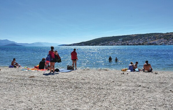 A pebbled beach with people sunbathing and swimming.