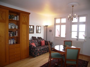 A cozy living room with a floral sofa, wooden cabinet, and a dining table with chairs.