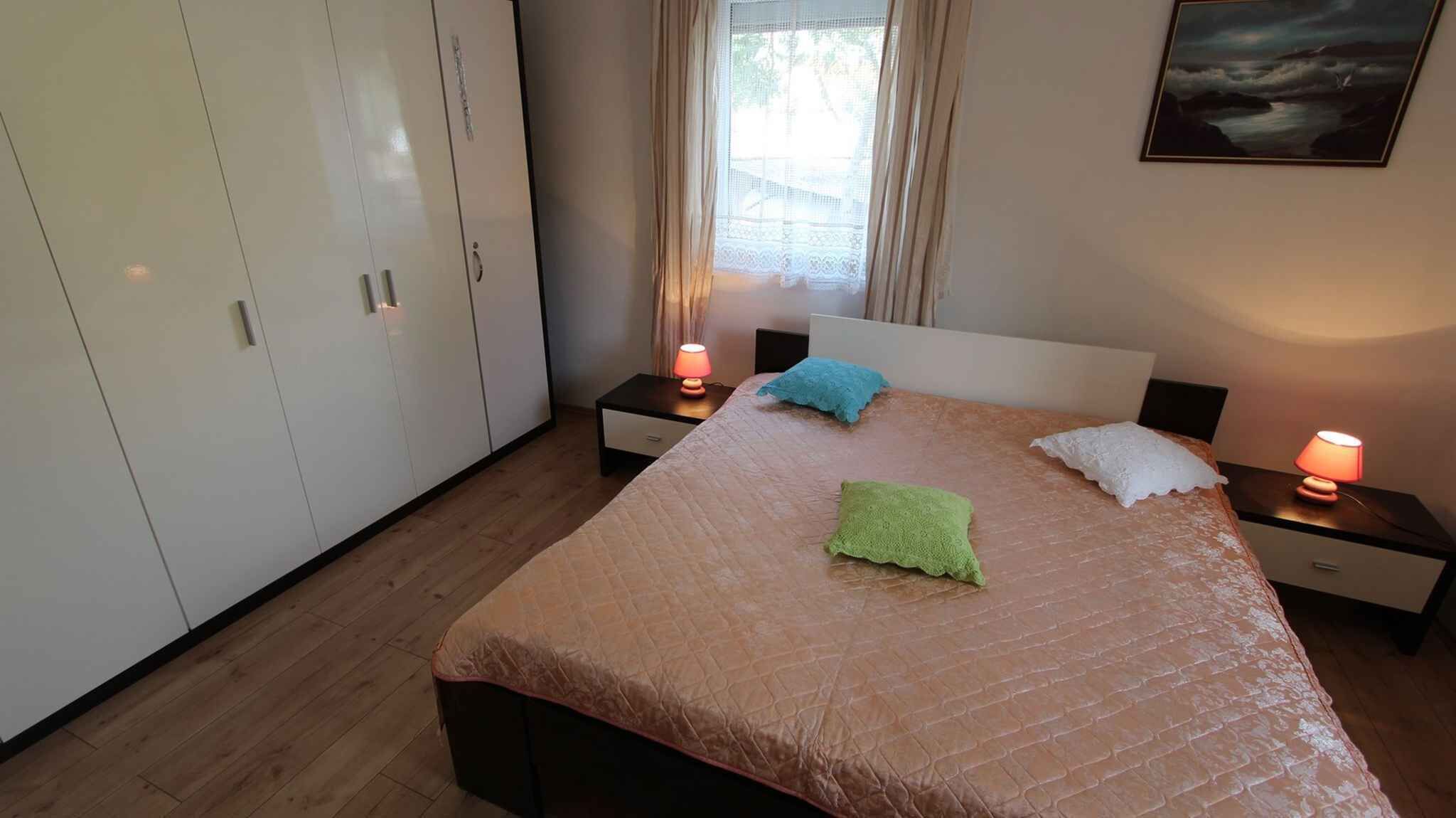 A bedroom with a bed, two bedside tables with lamps, a wardrobe, and a window with curtains.