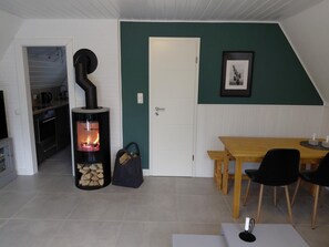 Un salon chaleureux avec une cheminée, un coin repas et une cuisine visible à travers une porte ouverte.