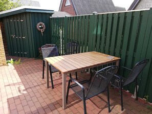 Un patio con una mesa de madera y cuatro sillas, una cerca verde y un adorno decorativo.
