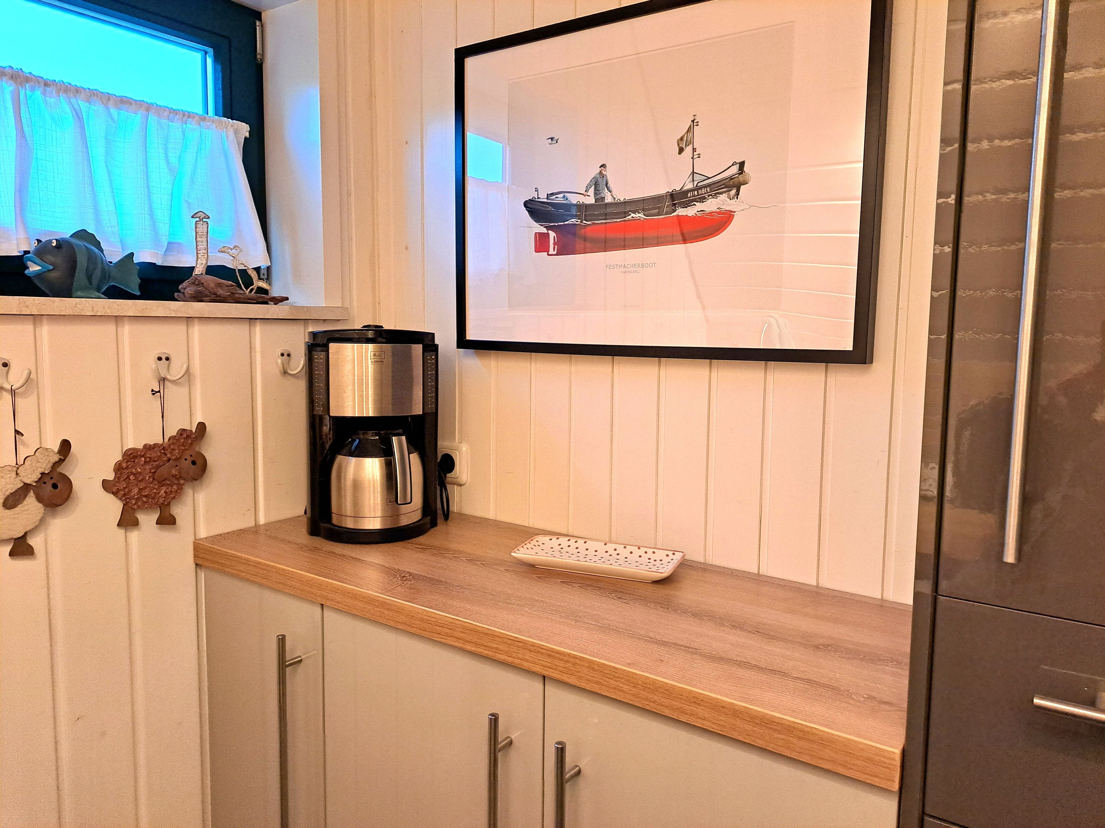 A kitchen with a coffee maker, a framed picture of a ship, and decorative sheep figures.