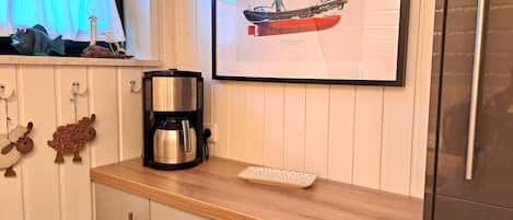 Una cocina con cafetera, un cuadro de un barco y figuras decorativas de ovejas.