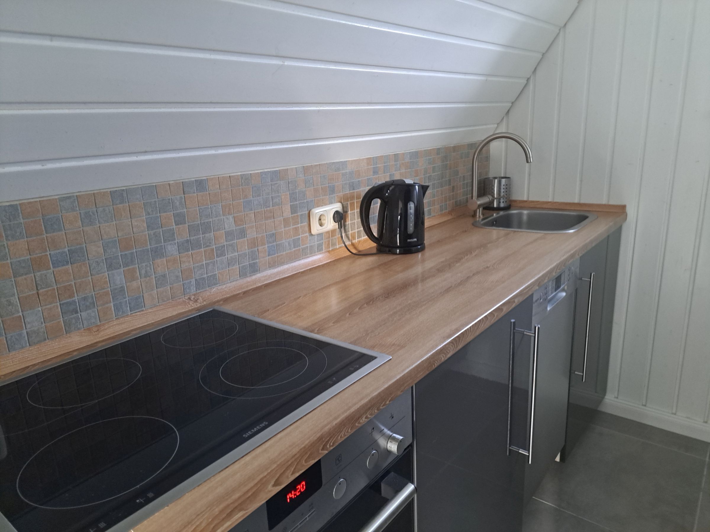 A modern kitchen with a wooden countertop, a black induction cooktop, a coffee maker, a sink, and a dishwasher.