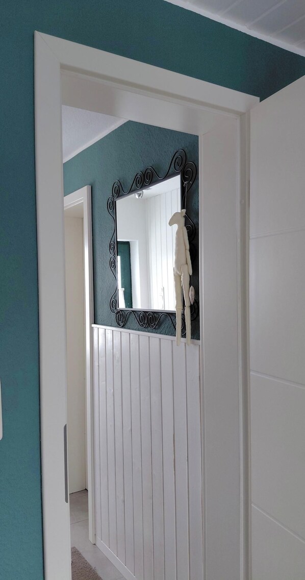 Quarto com paredes verde-água, porta branca e espelho com moldura decorativa.
