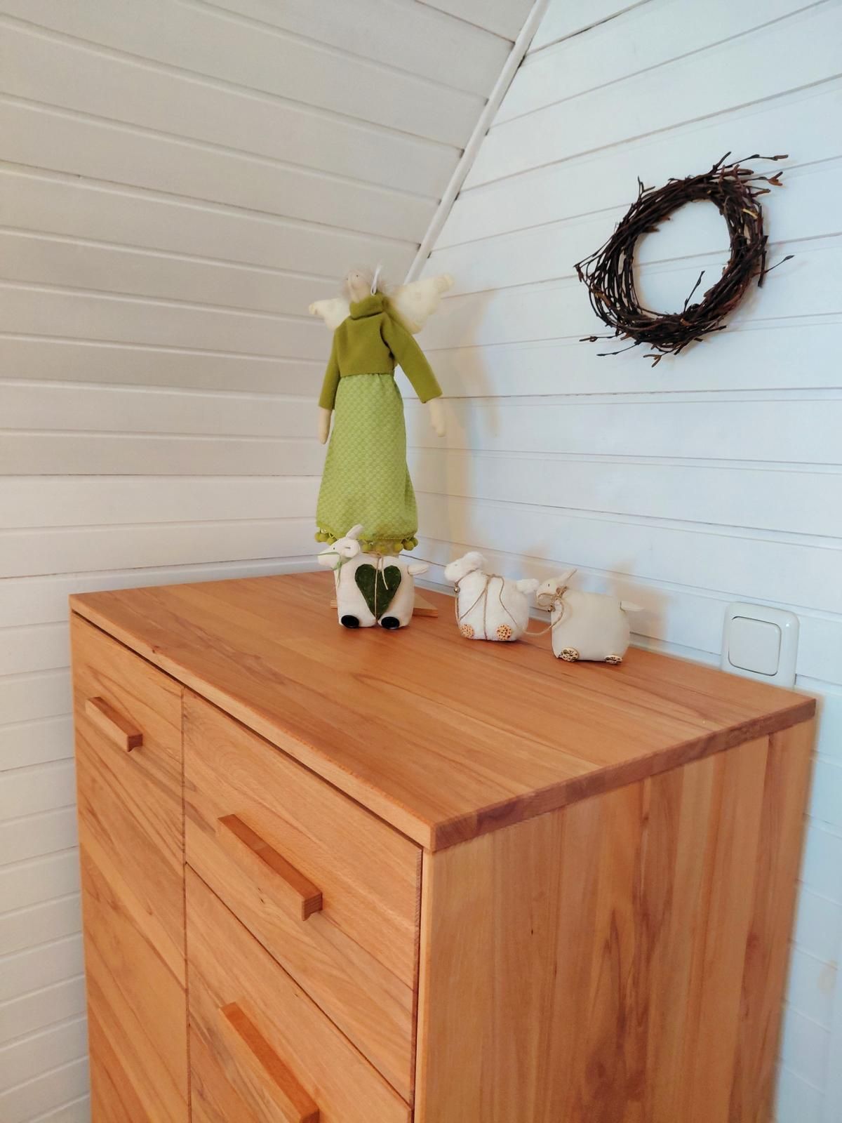 A wooden cabinet with drawers, a doll with a green dress, and a wreath on the wall.