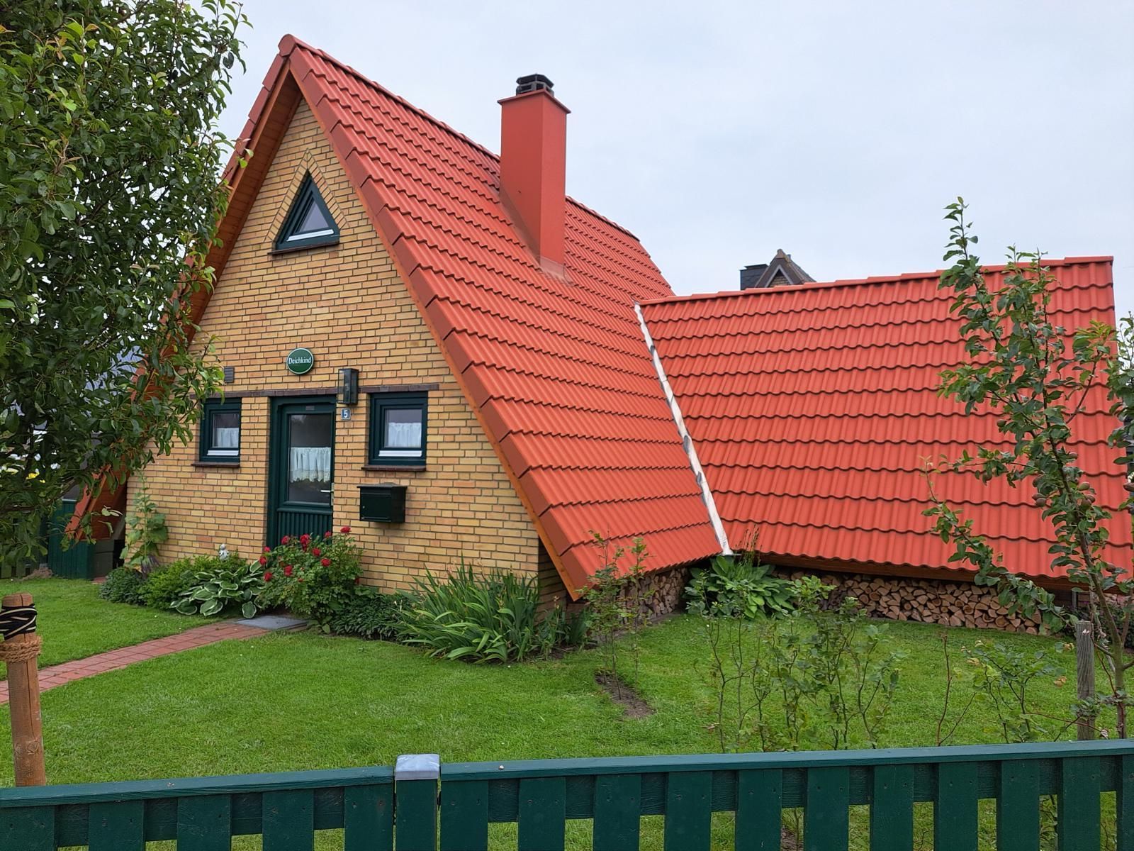 A house with a sloped red roof, a brick facade, and a small garden with a pathway leading to the entrance.