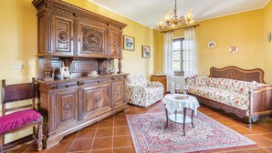 A room with a large wooden cabinet, a floral sofa, a small table with a white tablecloth, and a chandelier. - Cozy home in Aramengo (AT) (Aramengo (AT))