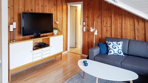 Een moderne woonkamer met een flatscreen televisie, een grijze bank, een witte salontafel en houten lambrisering.