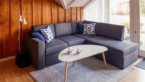 Een moderne woonkamer met een grijze modulaire bank, gekleurde kussens, een witte salontafel en een houten wand.