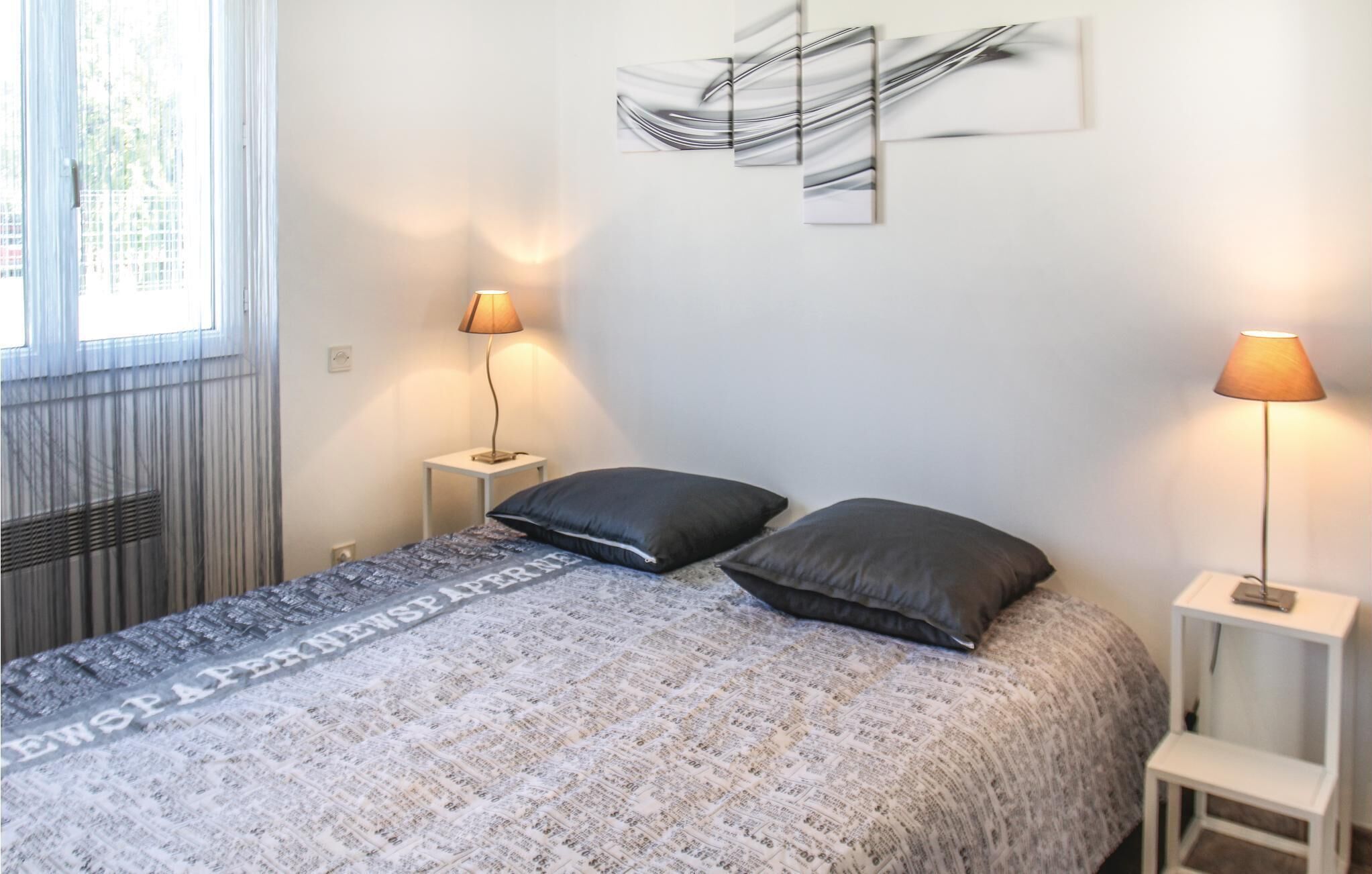A bedroom with a bed, two bedside lamps, a window, and abstract wall art.