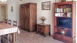 A dining area with a hexagonal tiled floor, a wooden table with chairs, a cabinet, a small side table with a vase of flowers, and a bookshelf with books and a television. - 3 bedroom nice home in La Faute sur Mer (La Faute sur Mer)