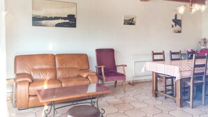 A living room with a brown leather sofa, a purple armchair, a wooden coffee table, and a dining area with a table and chairs. - 3 bedroom nice home in La Faute sur Mer (La Faute sur Mer)