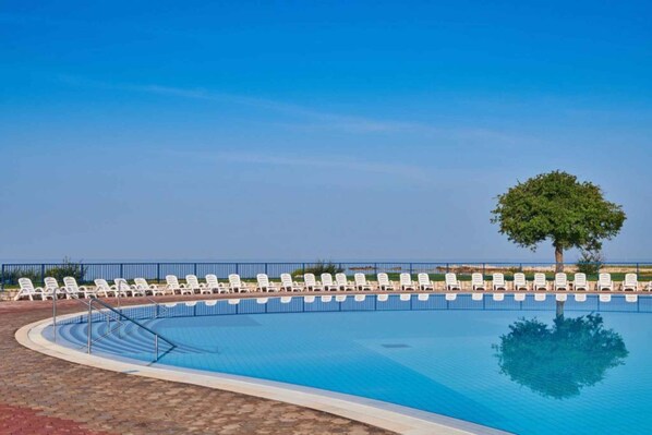 A swimming pool with white lounge chairs and a tree in the background.