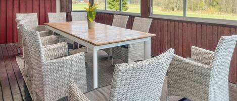 A covered outdoor dining area with wicker furniture and a wooden table.