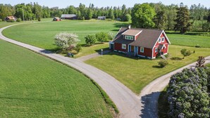 A red house with a sloped roof, surrounded by a green field and a curved road. - Amazing home in Bolmsö with sauna (Bolmsö)