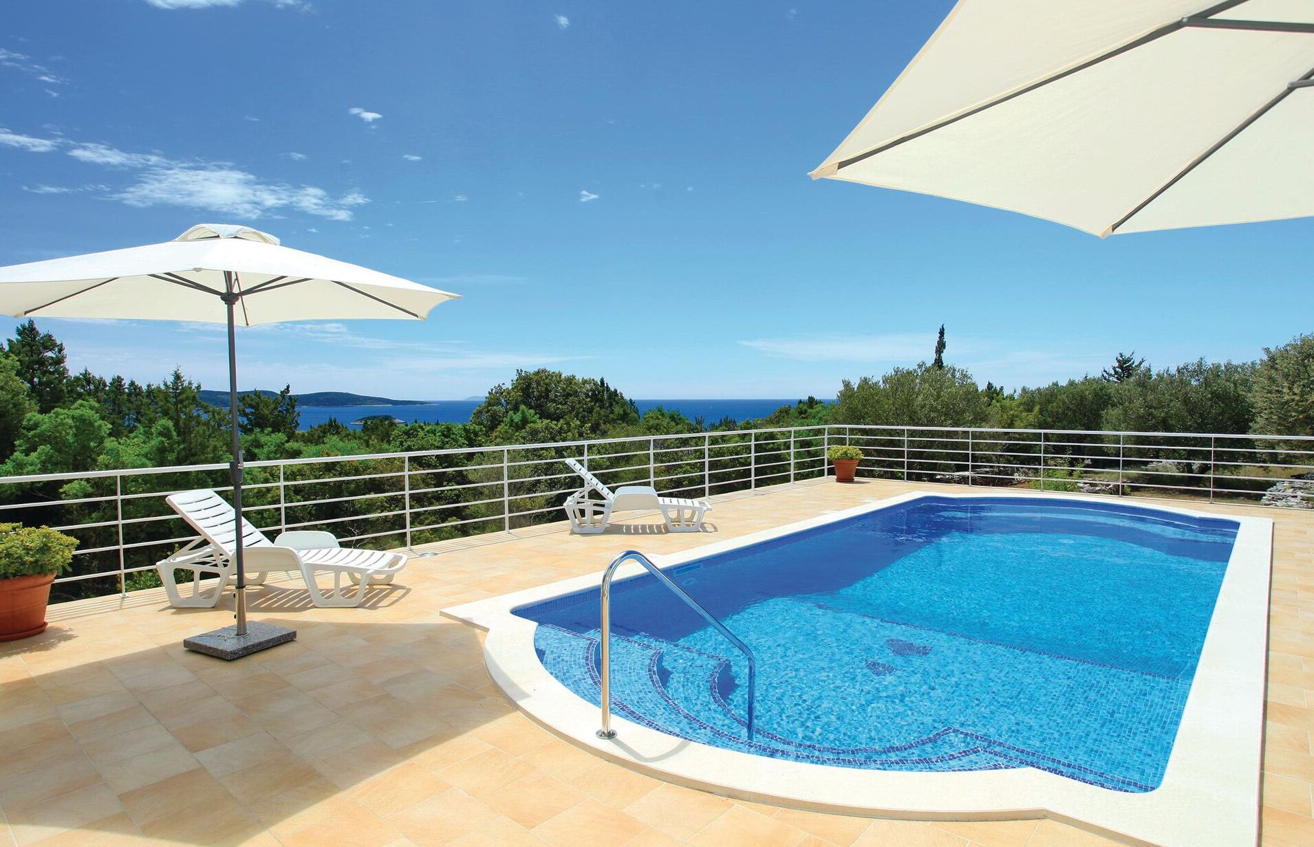A rooftop pool with a clear view of the sea, surrounded by lounge chairs and umbrellas.