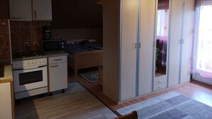 A compact kitchen with a stove, microwave, and cabinets. There is a bed with a wooden headboard and a large wardrobe with mirrored doors. - Studio with garden and internet (Balatongyörök)